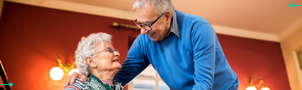 Elderly couple smiling at each other in their home.