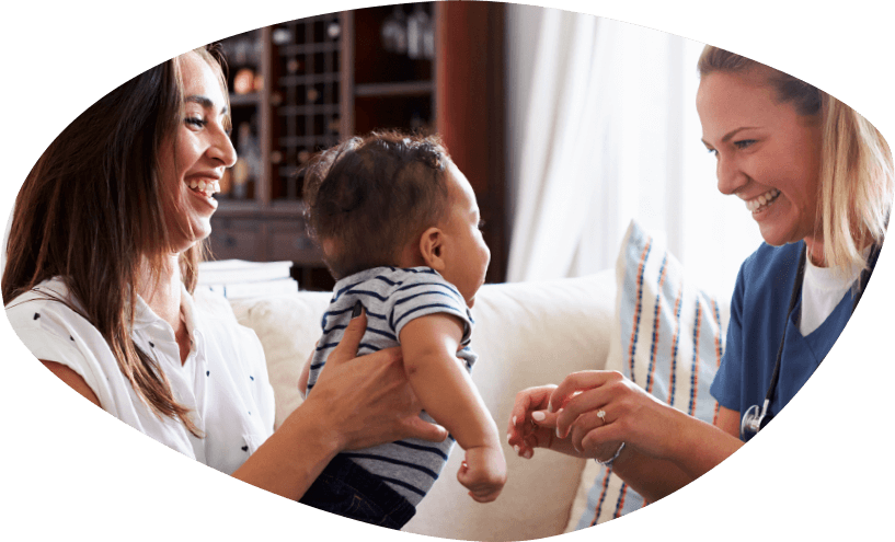 Smiling mother holding her toddler toward home visiting nurse who is reaching for the baby