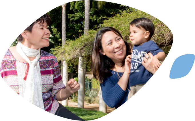 A smiling Asian mother holds her toddler facing his smiling grandmother