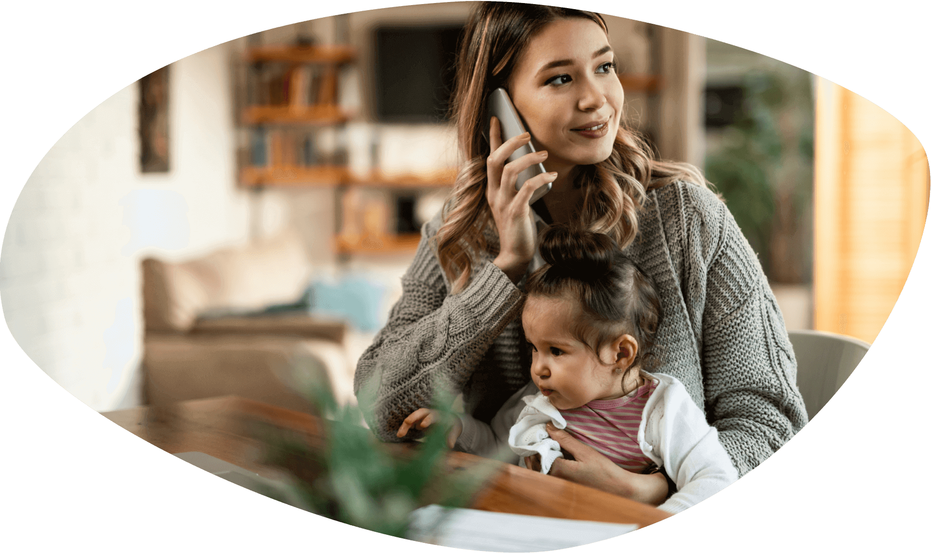 A young mother making a phone call is sitting by a table with her daughter on her lap